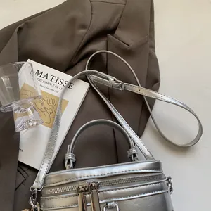 Detailaufnahme einer silbernen Mini-Box-Tasche mit Doppelreißverschluss auf dem Tisch