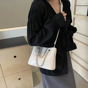 Detail of white glossy leather bucket bag featuring elegant silver metal chain accents