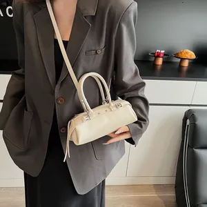 Detail of a creamy white cylindrical baguette bag with silver studs and slim shoulder strap