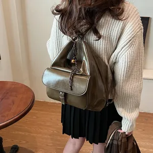 Detail view of olive green glossy leather backpack with decorative braided rope charm