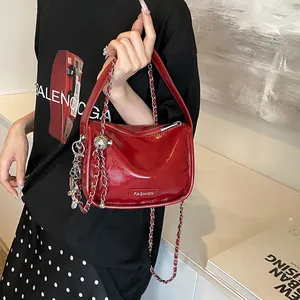 Detail of bright red patent leather handbag with silver chain charms and fashion label