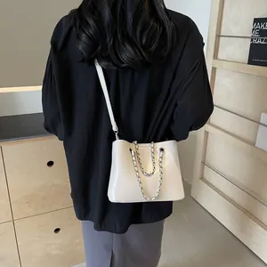 Model wearing a cream-white patent leather bucket bag with silver chain strap details