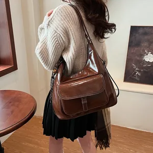 Detail of a brown glossy leather hobo bag with a front flap pocket and retro metal buckle
