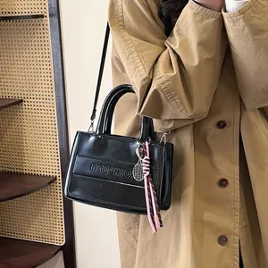 Glossy black tote bag with embossed logo on khaki coat model in retro autumn setting