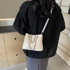 Detail view of cream white PU leather bag with metal chain strap worn by a model