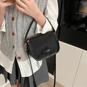 Detailansicht der schwarzen Umhängetasche mit Faltenstruktur und Bronze-Hardware am Model