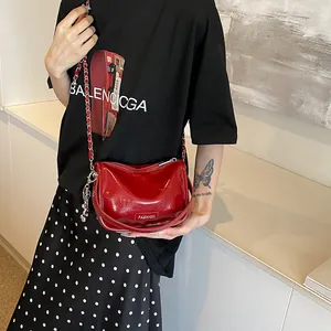 Detailed view of a red patent leather crossbody bag with a fashion logo and silver chain