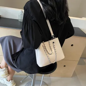 Detail of a white bucket bag with bold silver chains and a long leather shoulder strap