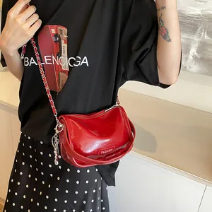 Red glossy leather semi-circle crossbody bag with chain strap worn by a model
