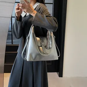 Chic silver metallic tote bag featuring a buckle strap and woven tassel on a model
