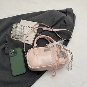 Pink matte PU Boston bag with lace bow and tennis racket charm against a grey blazer