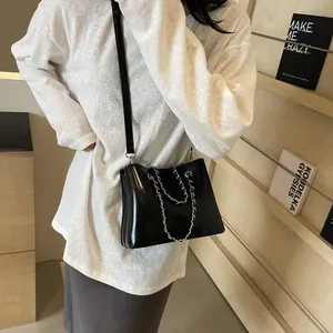 Detail of glossy black shoulder bag with silver chain handle and adjustable strap