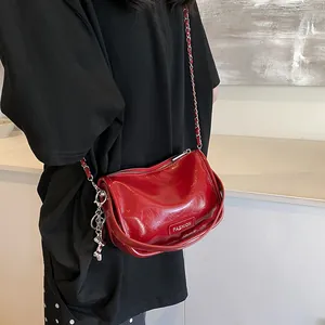 Detail of red patent leather crossbody bag with chain strap and fashion charm on model