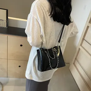 Detail of black leather bucket bag with silver chain handle and long strap on model