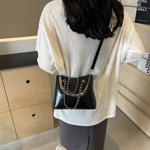 Detailed view of the shiny black crossbody bag with silver chains on a model back