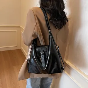 Detail of glossy black patent leather shoulder bag with metallic buckle and soft structure