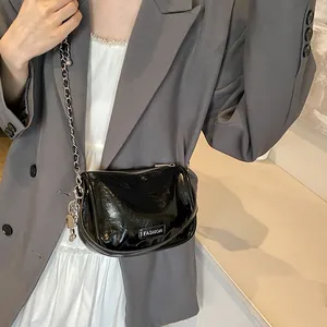 Close-up of black glossy crossbody bag featuring silver chain strap and fashion logo