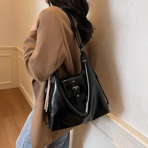 Detail view of glossy black faux leather shoulder bag with buckle strap on a model