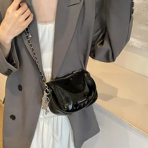 Detail of black patent leather crossbody bag with silver chain strap on grey blazer