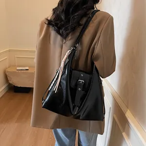 Detail of black glossy hobo bag with silver buckle and woven charm on a commuter outfit
