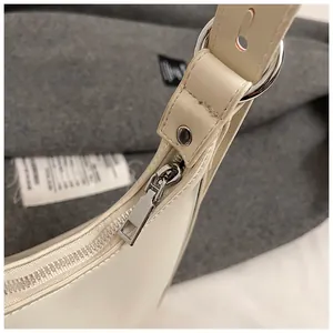 Detailed close-up of white half-moon bag with silver zipper and metallic ring hardware