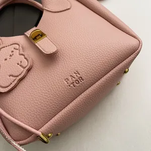 Détail du sac à main en cuir grainé rose avec pieds en métal doré et logo PAN TOR