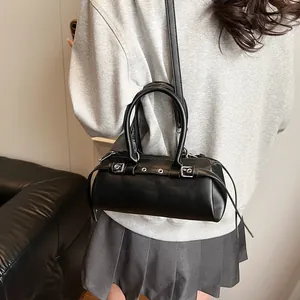 Detail of a black cylindrical baguette bag with metallic buckle strap and smooth PU finish