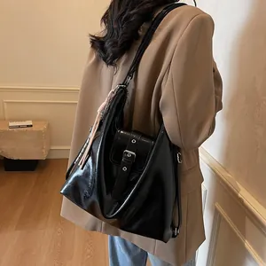 Rear view of model wearing a large black patent leather hobo bag with tassel detail