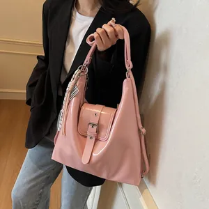 Detailed view of pink leather shoulder bag with buckle and decorative tassel on model