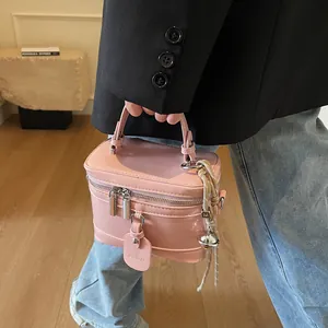 Detailansicht einer rosa Box-Handtasche mit Ledergriff und Glocken-Anhänger