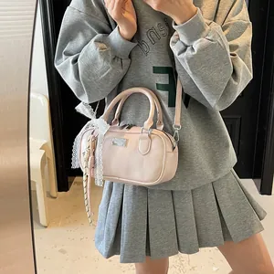 Pink bowling style crossbody bag with lace bow accessory shown in a casual lifestyle setting