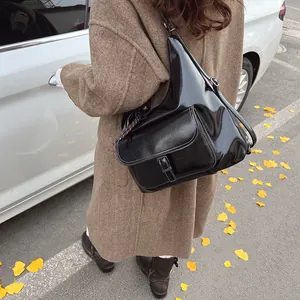 Side view of a glossy black leather crossbody bag worn with a brown autumn coat