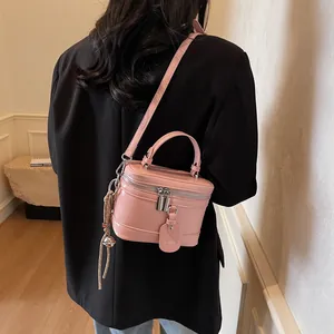 Detailansicht einer rosa Koffer-Handtasche mit Griff und Quaste an einem Modell