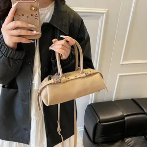 Detail of minimalist beige baguette bag with silver buckles worn with a leather jacket