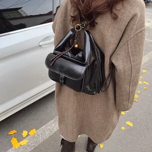 Close-up of black glossy leather backpack with metal buckle on brown wool coat background