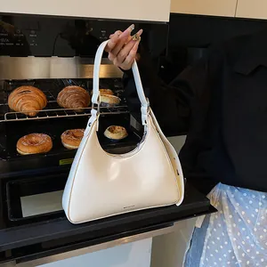 Close-up of white leather hobo bag with 'NO FILTER' text against a bakery background