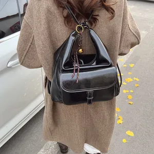 Outdoor view of a black glossy backpack with white stitching and a small bell charm