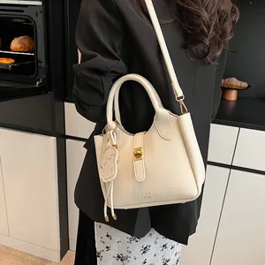 Détail du sac seau en cuir beige avec fermoir doré et pendentif ours décoratif