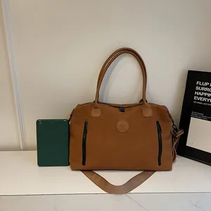 Brown faux leather duffel bag with dual handles and side pockets on marble surface