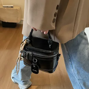 Detail einer schwarzen glänzenden Vanity-Tasche mit Metall-Reißverschlüssen und Riemen