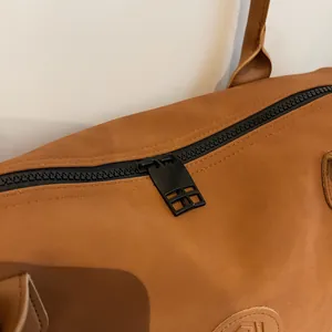 Detail of matte brown travel bag featuring dual black metal zippers and fine leather texture