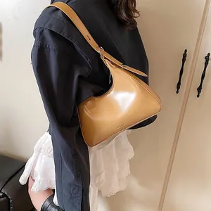 Detail of caramel half-moon shoulder bag featuring no filter embossed text and silver buckles