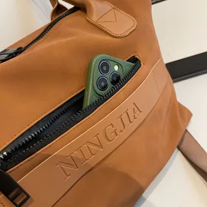Detail of the side zipper pocket on a brown leather travel bag holding a mobile phone