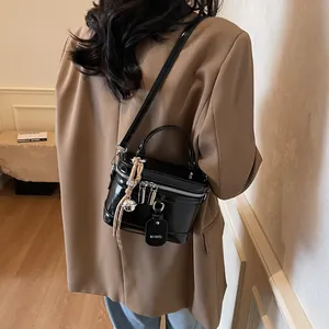 Detailansicht einer glänzenden schwarzen Box-Tasche mit Metallglocke und Markanhänger