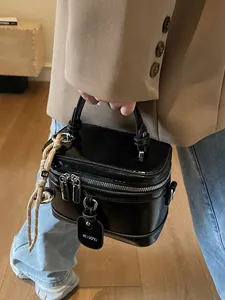 Glänzende schwarze Lacktasche in Boxform mit silbernen Reißverschlüssen und Anhänger