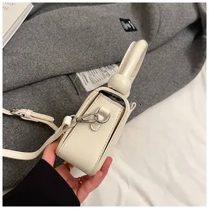 Vue latérale d'un sac à bandoulière en cuir verni blanc crème avec poignée nouée