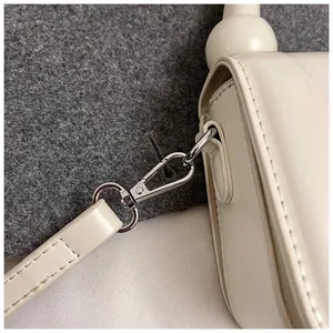 Gros plan sur le fermoir métallique argenté et les coutures de ce sac à main blanc crème