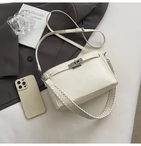 Detail view of cream square crossbody bag featuring silver lock and dual strap design