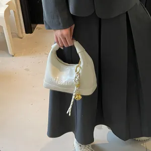 Detail of cream faux leather handbag featuring embossed lettering and gold bell charm