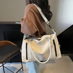 Close-up of beige travel tote bag with shoulder strap and embossed circular logo detail